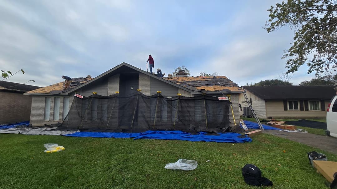 Workers installing a new roof on a house with tarps and scaffolding.