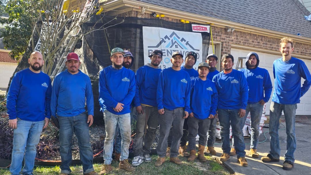 Renovation team in blue shirts stands in front of a home with a company banner.