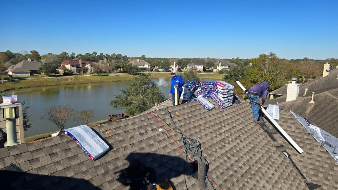Roofers installing shingles on a house near a lake on a clear sunny day.