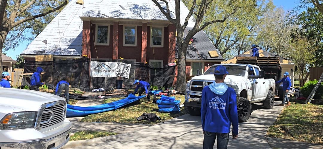 Roofing crew working on a house renovation with blue uniforms and vehicles in a suburban area.