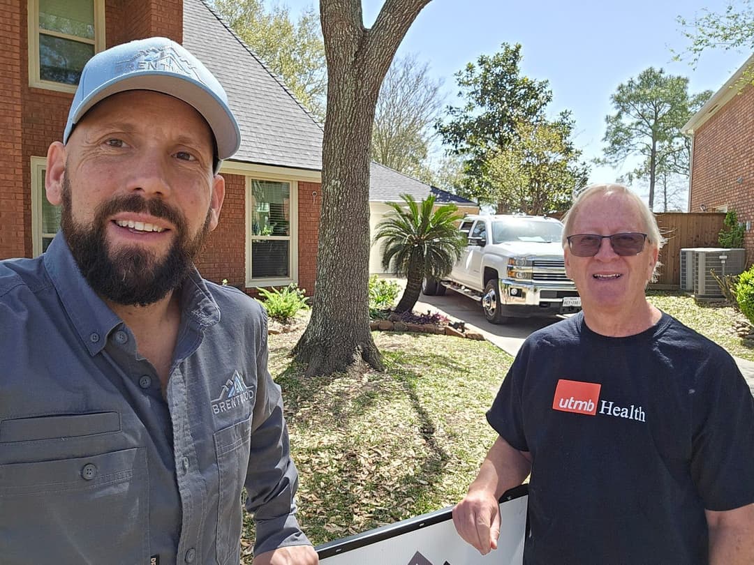 Two men pose outside a house with a truck in the background, promoting a local service.