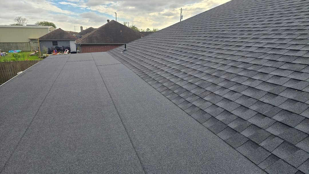 Aerial view of a residential roof with grey shingles and cloudy sky.