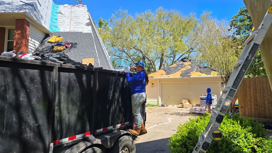 Roofing contractor working on a home renovation with a debris trailer in the driveway.