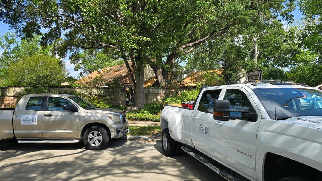 Two service trucks parked outside a home surrounded by greenery and trees.
