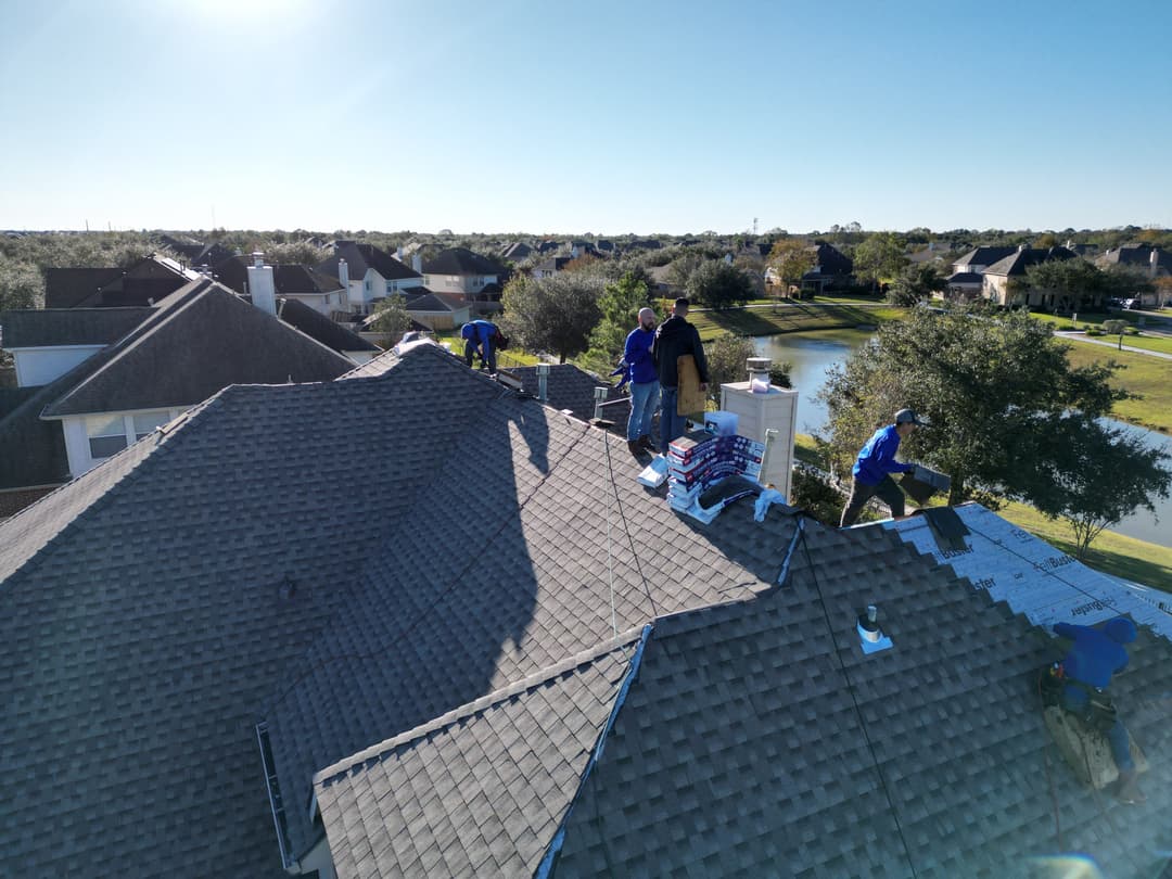 Roofing crew applying shingles on a residential home under clear blue skies.