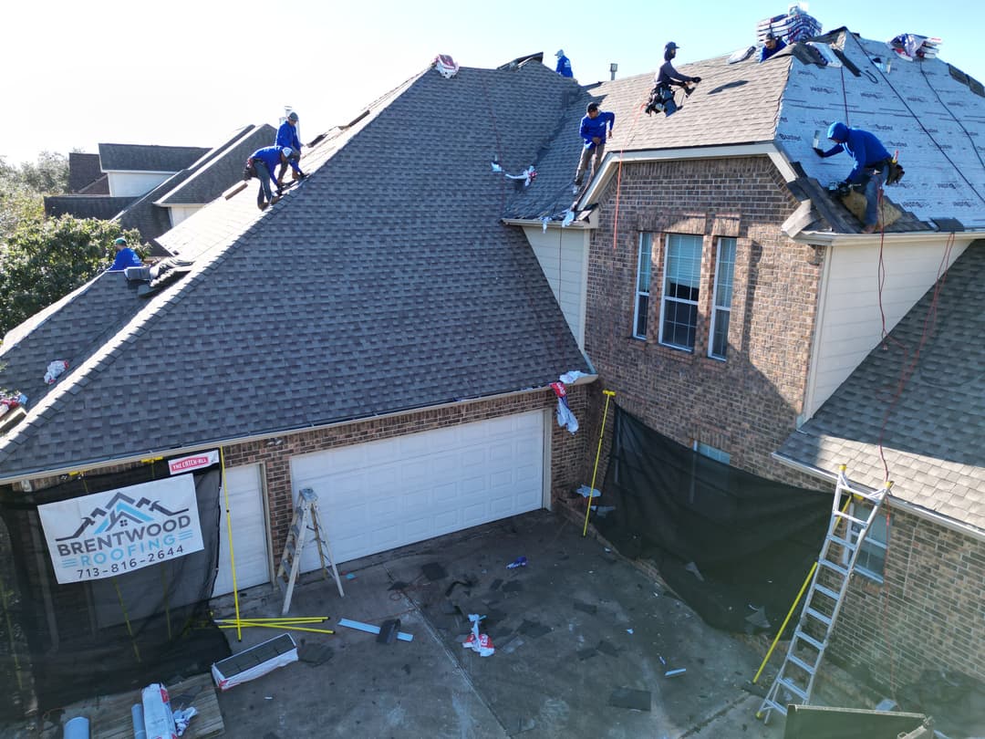 Roofing crew installing shingles on residential home with tools and equipment visible.