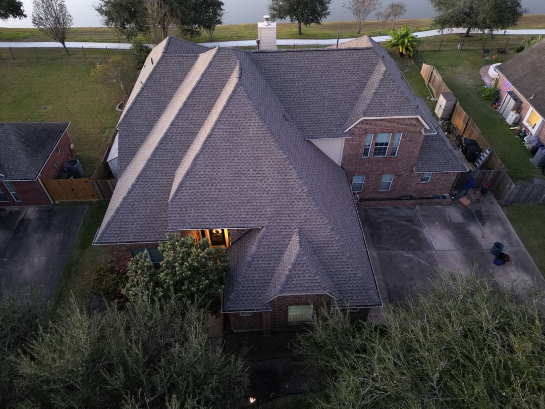 Aerial view of a residential home with a gabled roof and landscaped yard near a waterway.