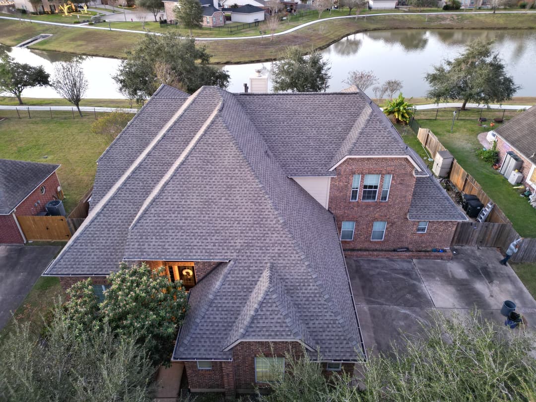 Aerial view of a brick house with a sloped roof and a pond in the background.