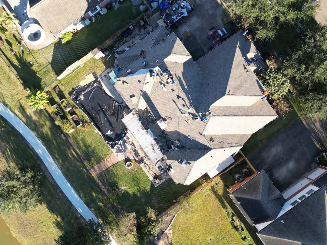 Aerial view of a residential home with workers repairing the roof and surrounding greenery.