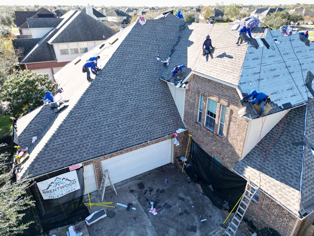 Roofing crew working on a residential home, installing shingles on a sloped roof.