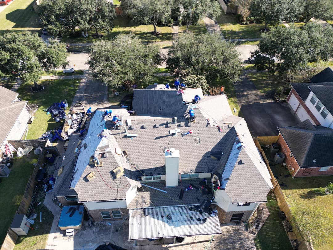 Aerial view of a house under roof repair with workers and equipment on the roof.