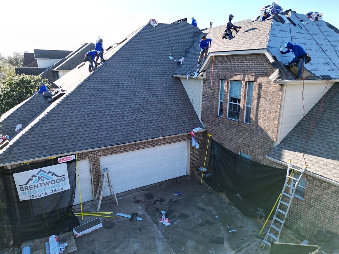 Roofing team installing shingles on a house, with tools and materials scattered below.