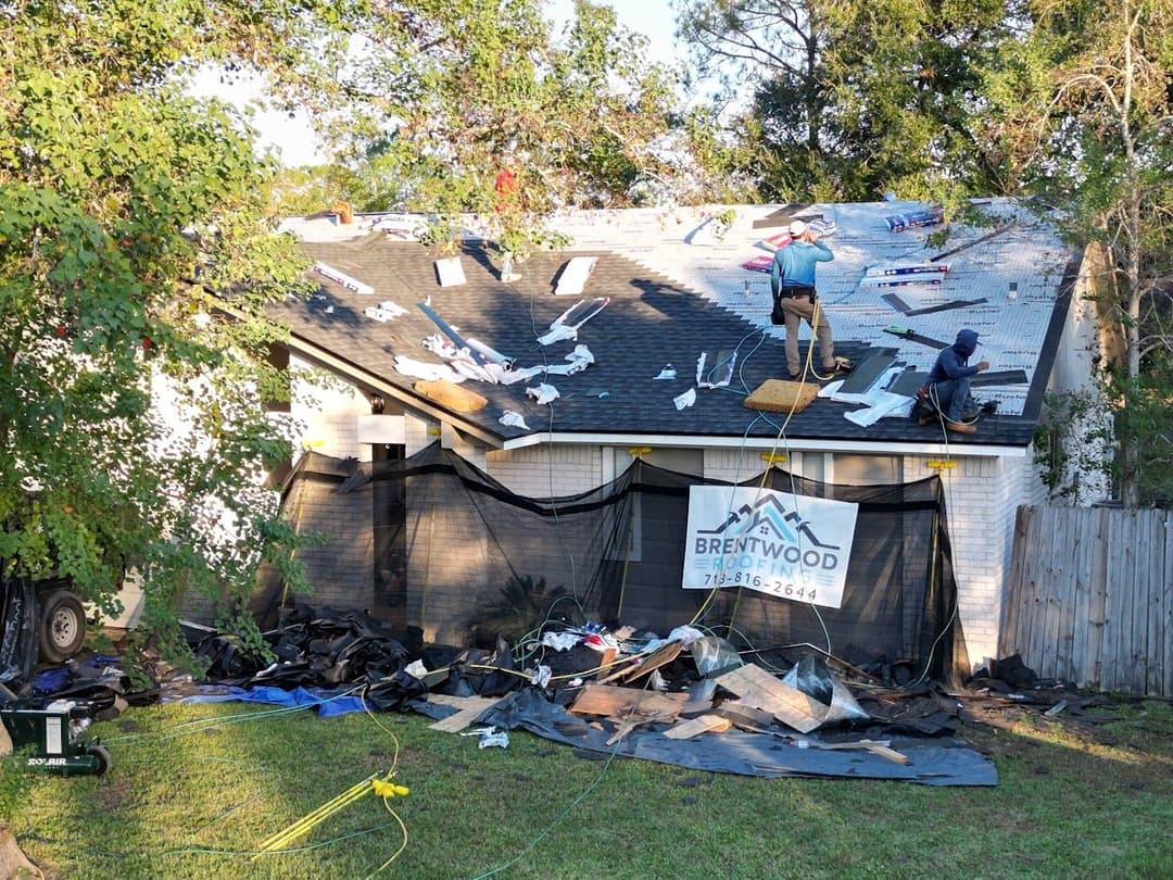 Roof repair in progress with workers applying shingles and debris on the ground. Brentwood Roofing.
